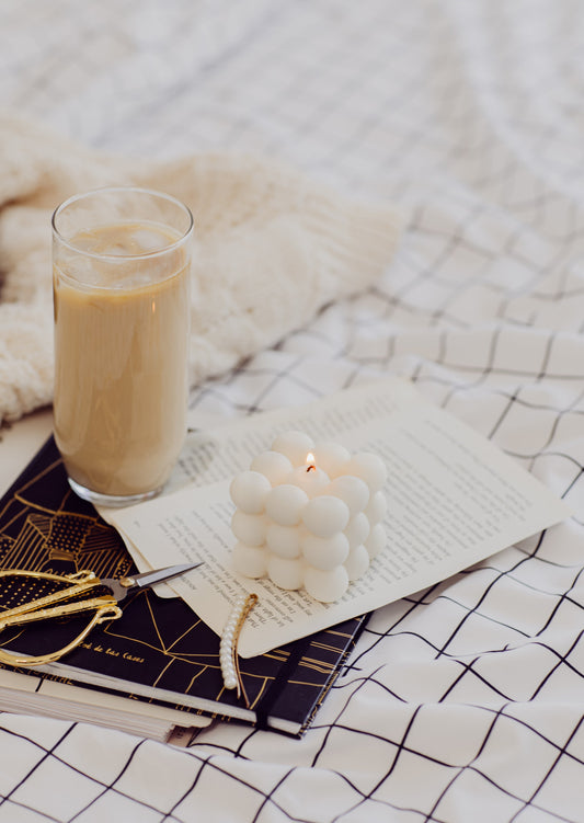 a lit candle with an iced coffee and a pair of scissors next to it