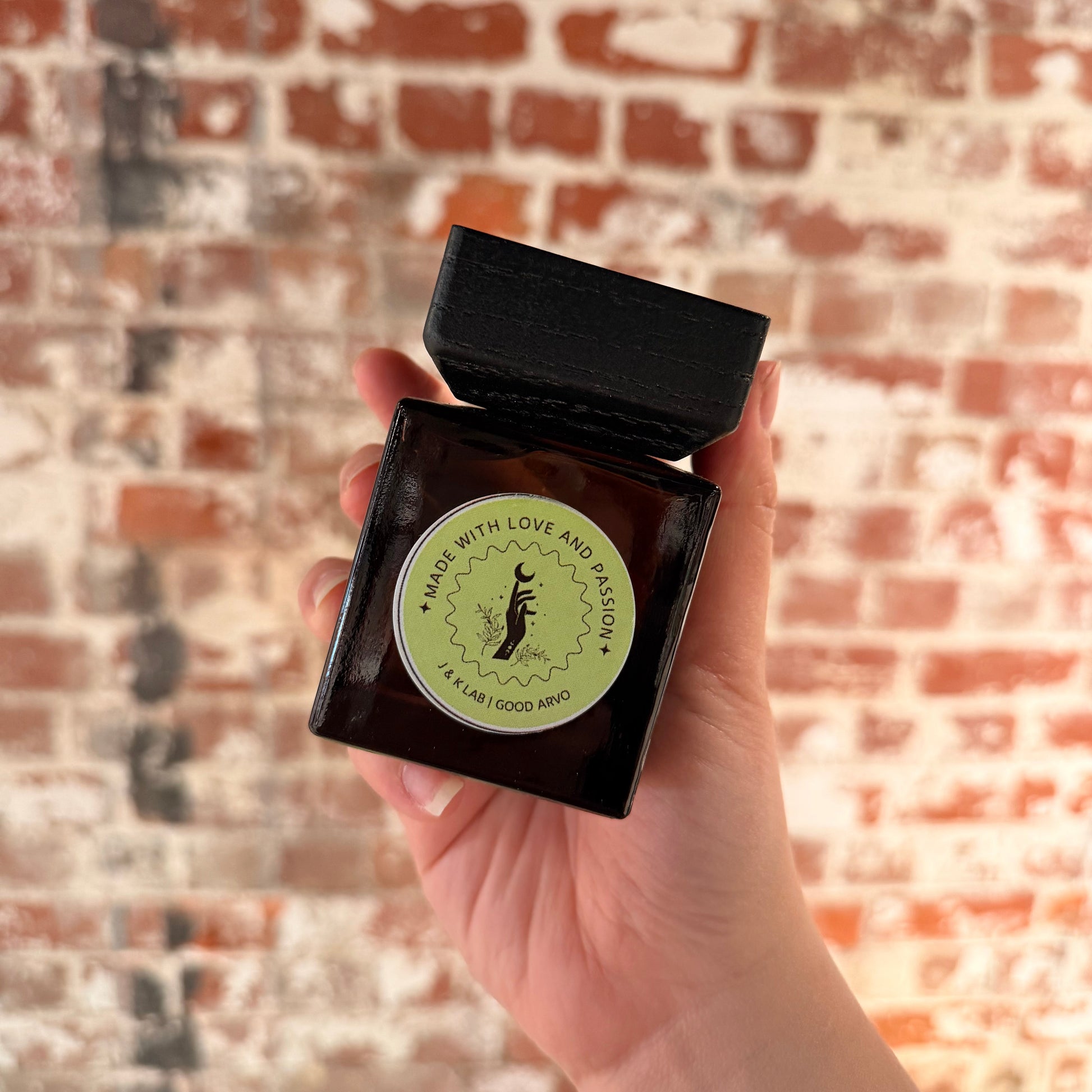 Reed diffuser in a dark glassware with a square wooden lid and lime green round label. 