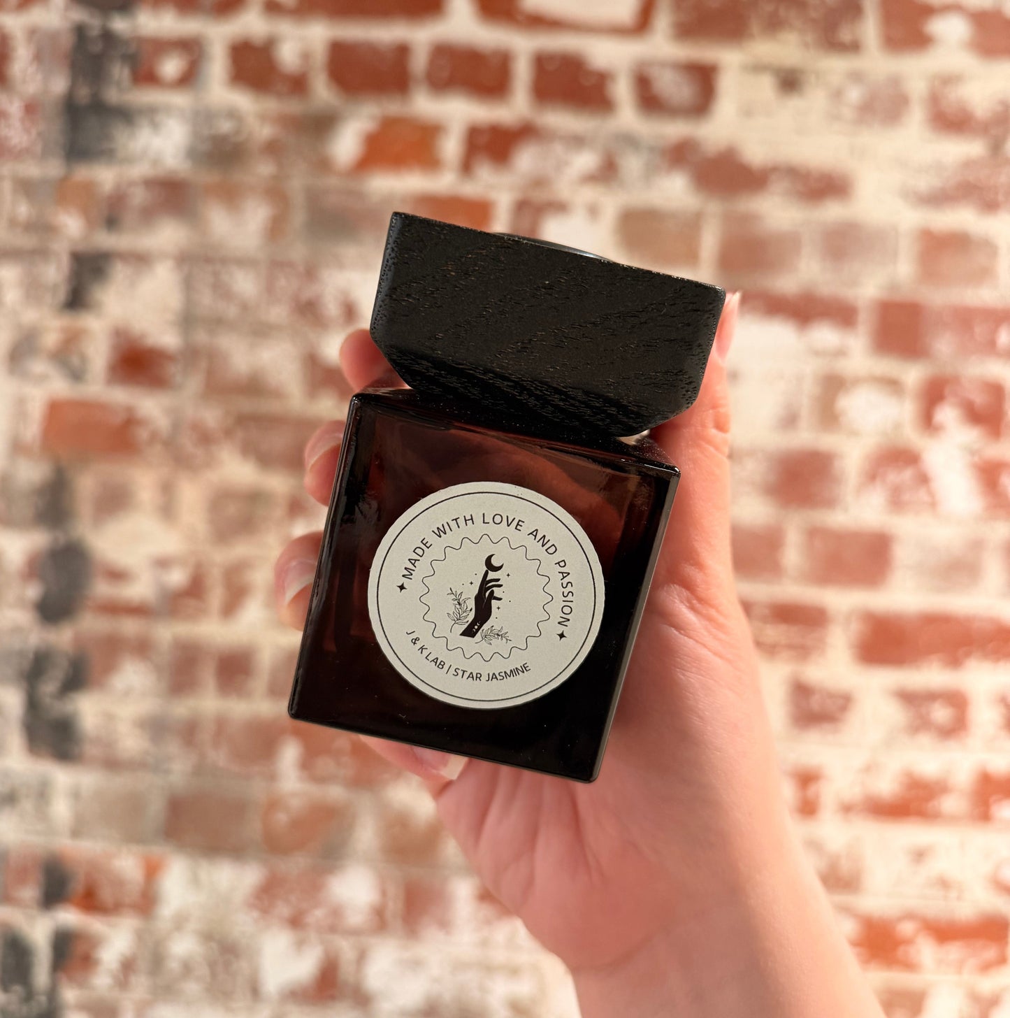 Reed diffuser in a dark glassware with a square wooden lid and white round label. 