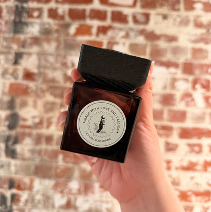 Reed diffuser in a dark glassware with a square wooden lid and white round label. 